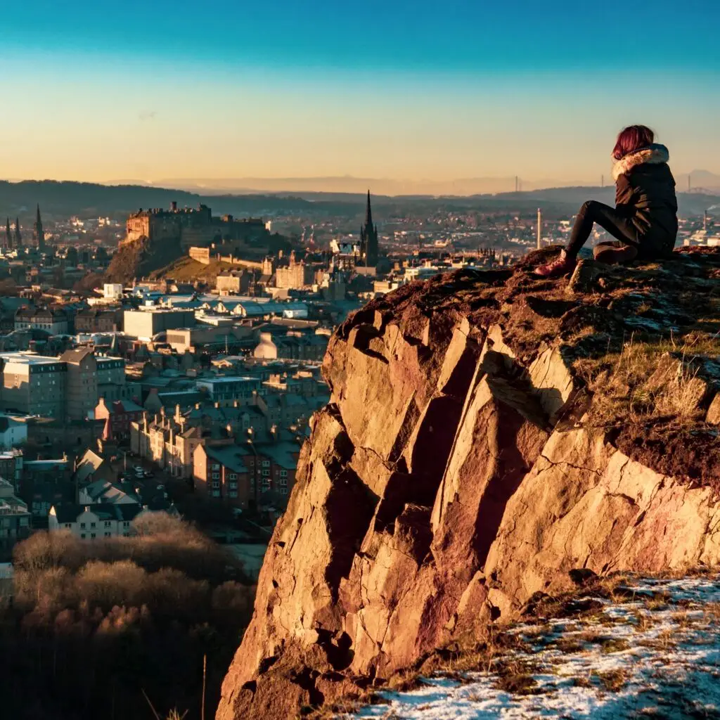 Woman looking across Edinburgh from a rocky viewpoint at sunset