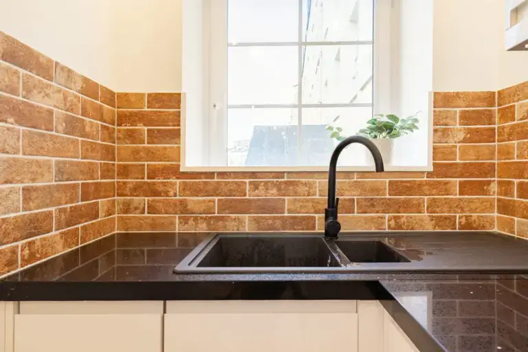 Kitchen sink beneath a window with exposed brick surrounds