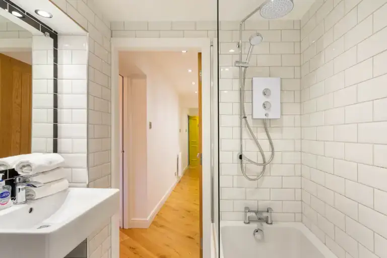 White-tiled shower room opening onto an apartment hallway