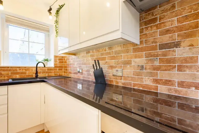 White kitchen with exposed brick walls and dark worktops