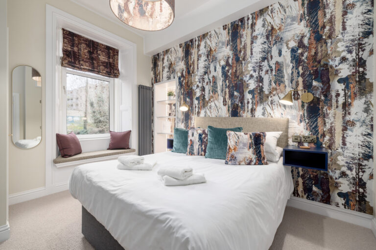 Guest bedroom with patterned wallpaper and a cushioned window seat