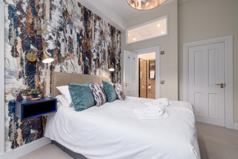 Double bedroom with abstract wallpaper and teal cushions