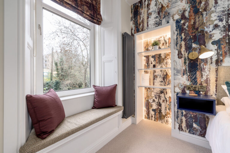 Cushioned window seat beside a patterned bedroom feature wall