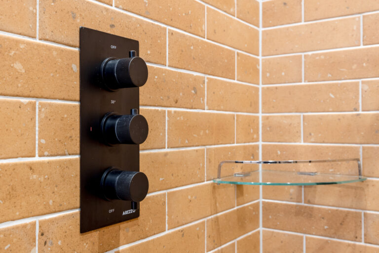 Black shower controls against ochre wall tiles