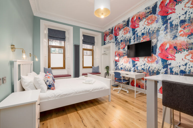 Double bed beside a colourful floral feature wall and kitchenette