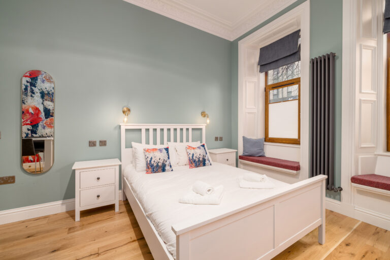 Studio bedroom with white bed frame and a desk by the window