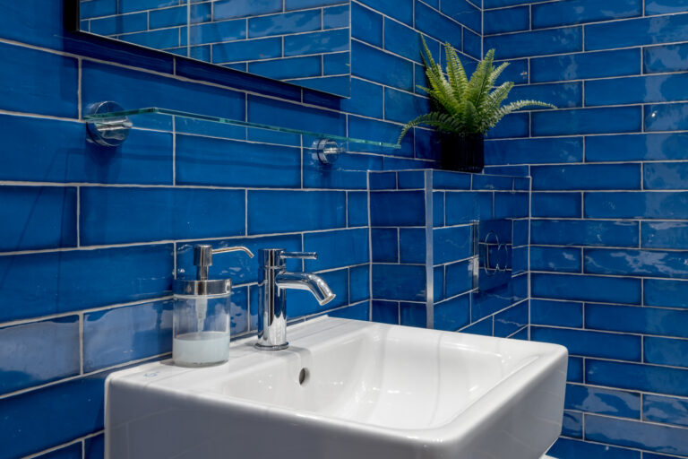 White bathroom basin beneath a mirror against blue tiles
