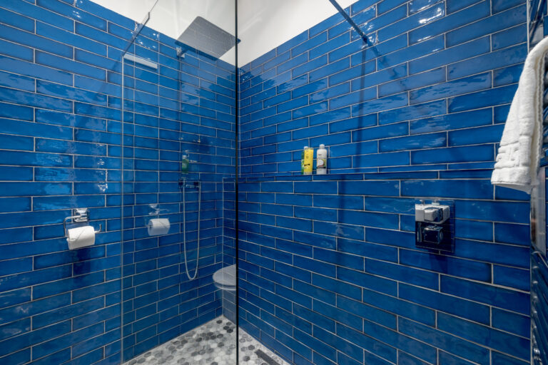 Blue-tiled walk-in shower with toiletries on a shelf