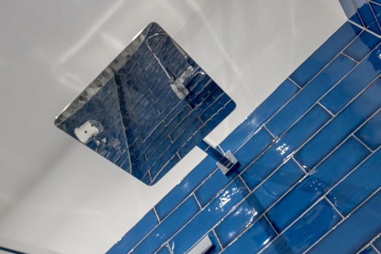 Square rainfall shower head in a blue-tiled shower