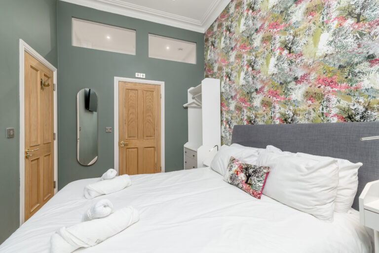 Guest bedroom with floral wallpaper and a grey upholstered headboard