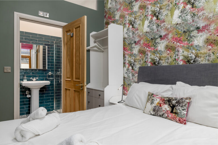 Double bed beside a floral feature wall and open bathroom door