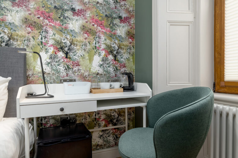 Dressing table and green chair beside floral wallpaper