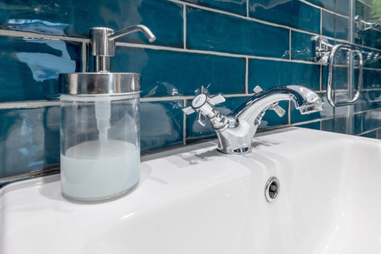 Bathroom basin and soap dispenser against teal tiles