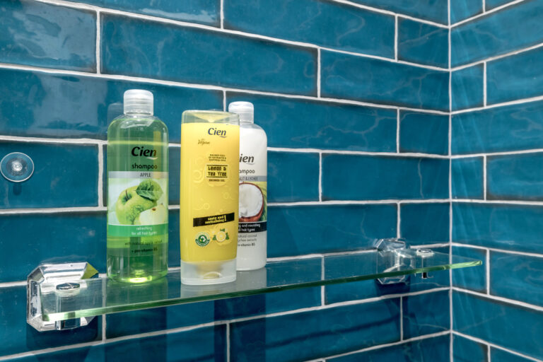 Toiletries on a glass shelf against teal bathroom tiles