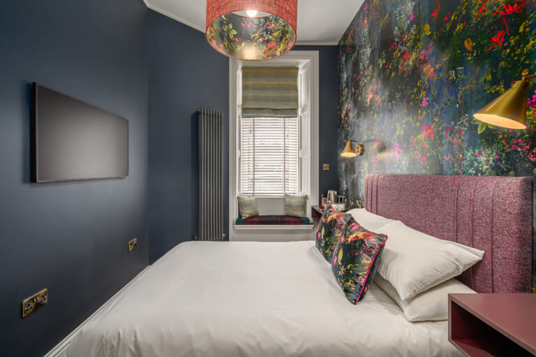 Double bed with a pink headboard beside a tall window