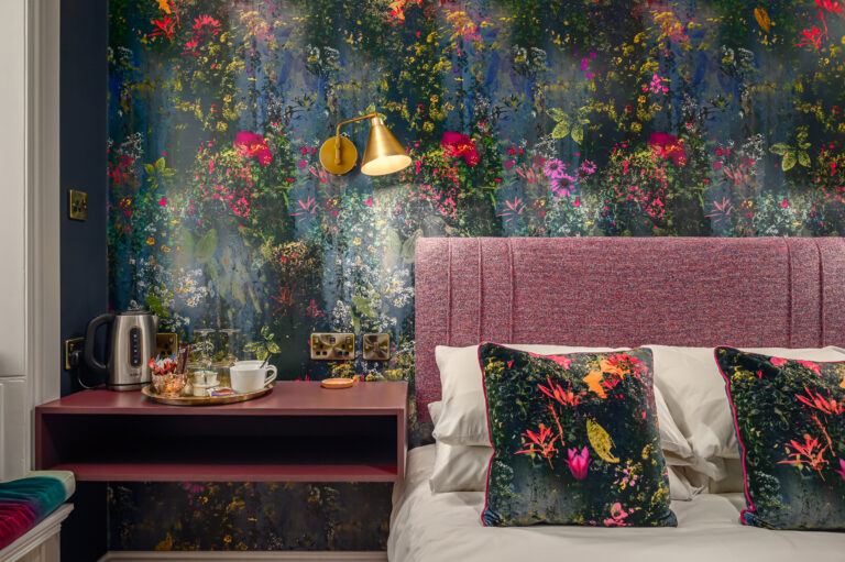 Pink upholstered headboard beneath a floral feature wall