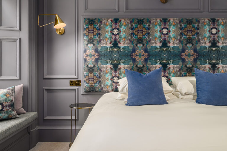 Double bed with blue cushions beneath a patterned feature wall