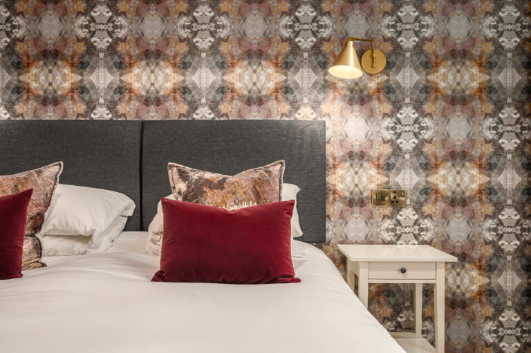 Red velvet cushions on twin beds beside patterned wallpaper