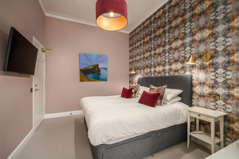 Guest bedroom with patterned wallpaper and red cushions