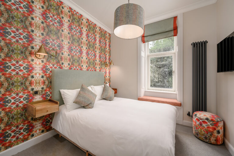 Double bed beneath a patterned feature wall beside a tall window
