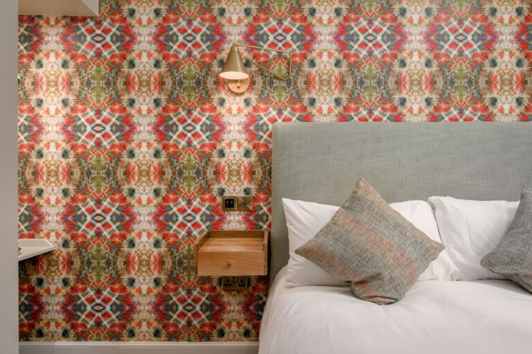 Grey upholstered headboard against a colourful patterned feature wall