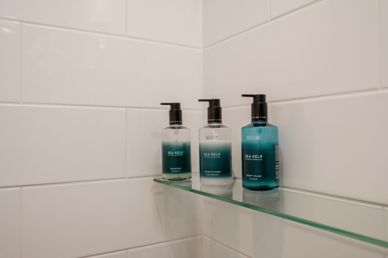 Shower toiletries on a glass shelf against white tiles