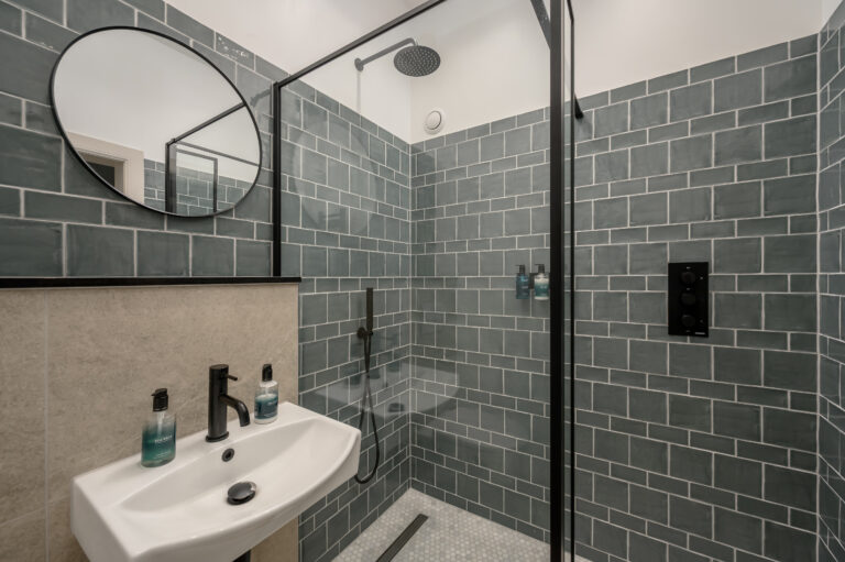 Grey-tiled shower room with a round mirror and white basin