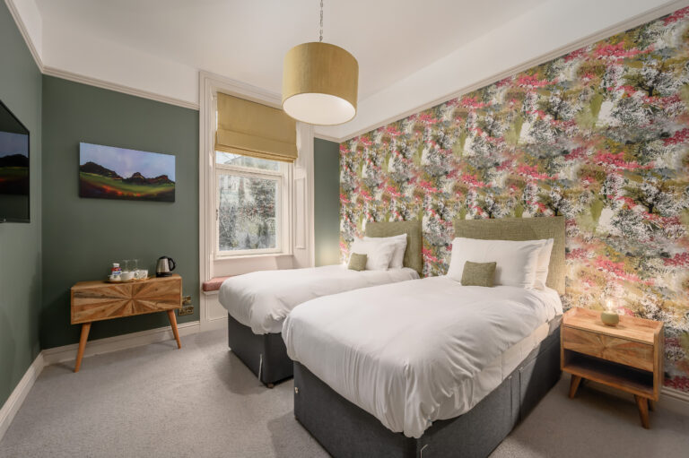 Twin beds beside a floral feature wall and green-painted walls