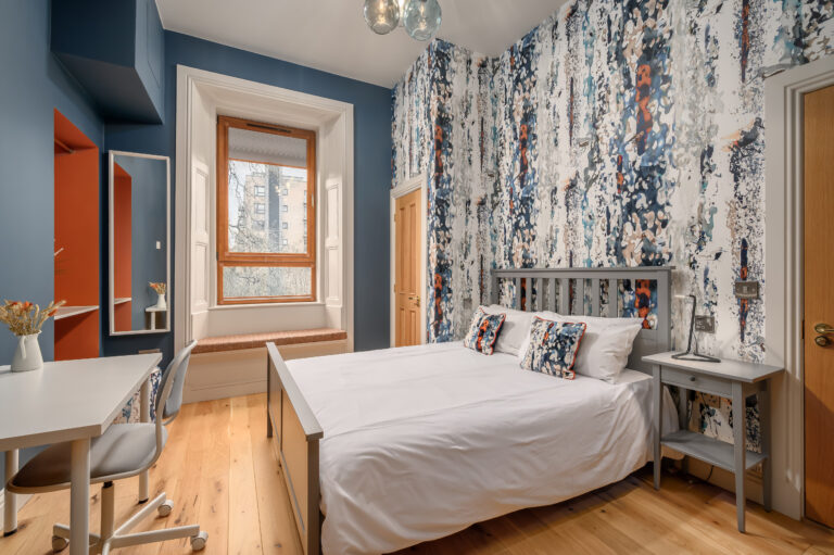 Studio bedroom with patterned cushions and a desk by the window