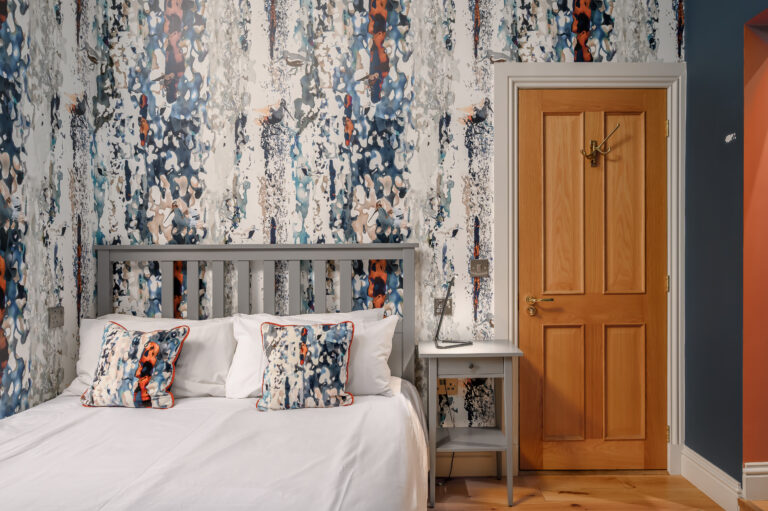Double bed beneath patterned wallpaper beside a wooden door