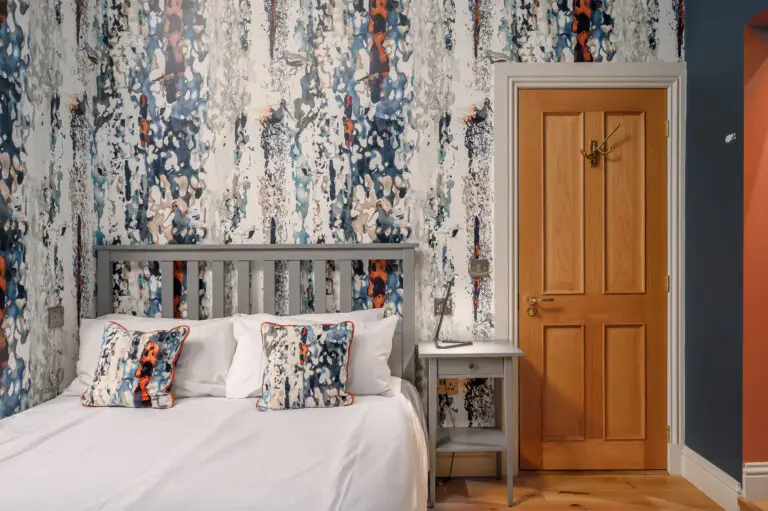 Double bed beneath patterned wallpaper beside a wooden door