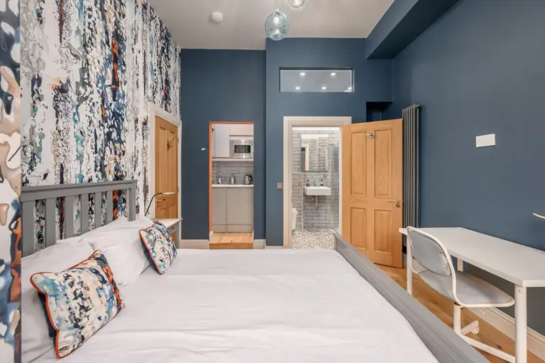 Blue-walled studio bedroom with patterned wallpaper and a desk