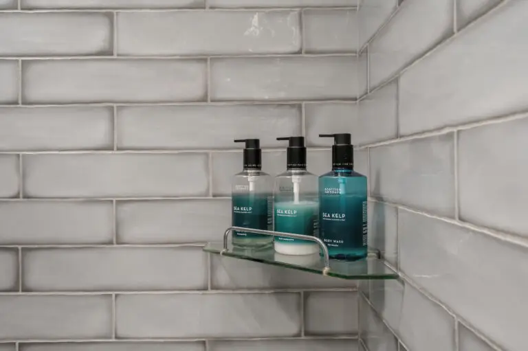 Toiletries on a glass shelf against grey bathroom tiles