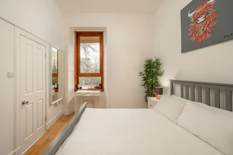White bedding and grey headboard beside a wooden-framed window