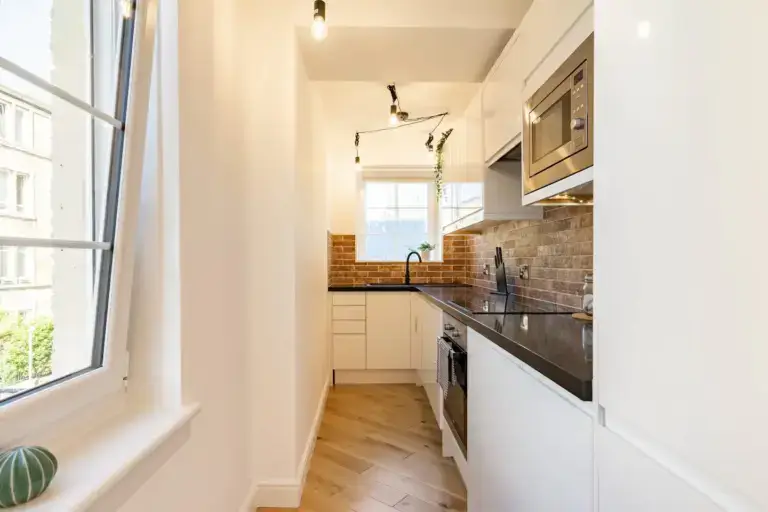 Apartment kitchen with white cupboards and a window above the worktop