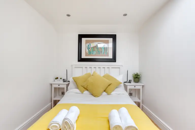 Double bed with yellow cushions in a white apartment bedroom