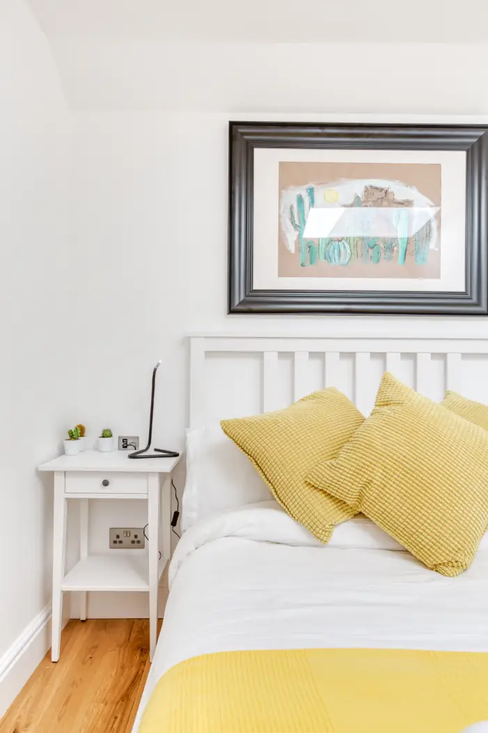 Double bed with yellow cushions beneath framed artwork