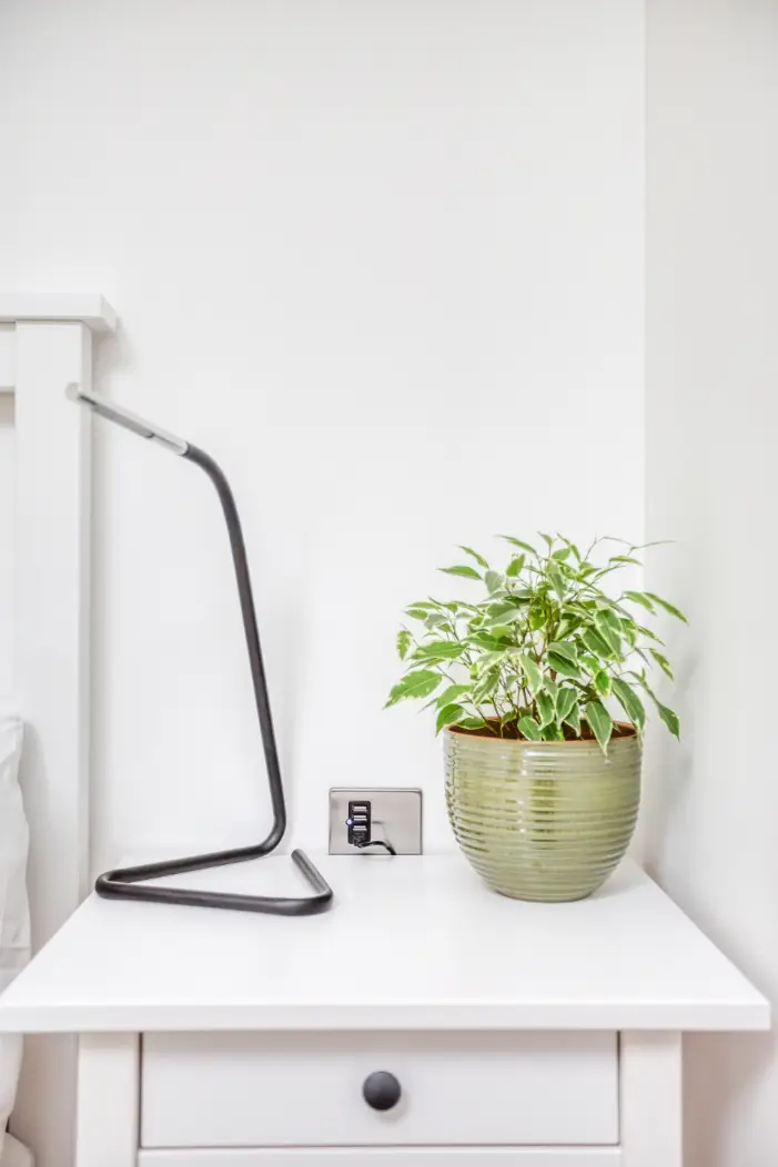 White bedside cabinet with a reading lamp and potted plant