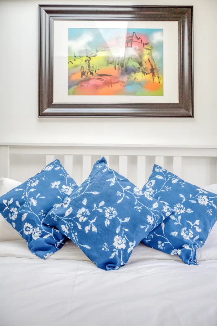 Blue floral cushions on a white bed beneath framed artwork