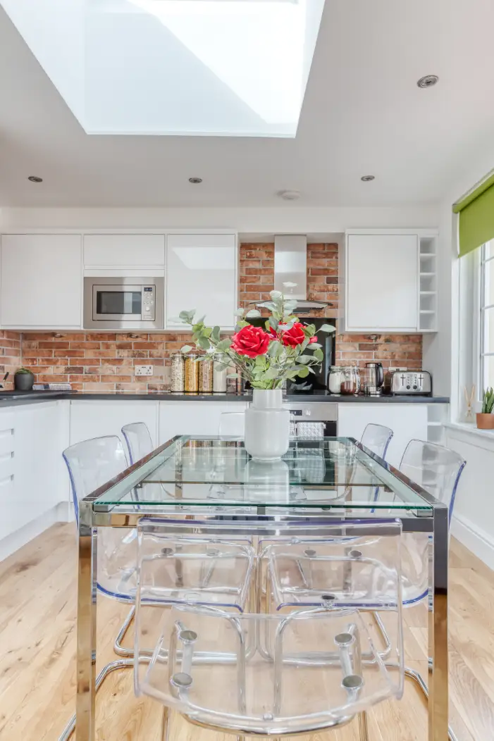 Glass dining table beneath a skylight in an open-plan kitchen