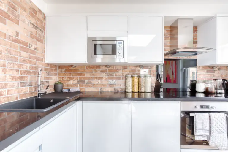 White fitted kitchen with an oven and brick splashback