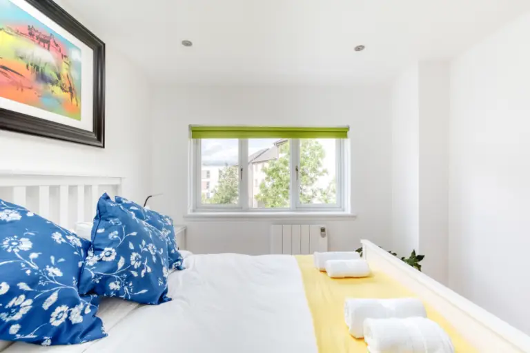 Double bed with blue cushions beside a window with a green blind
