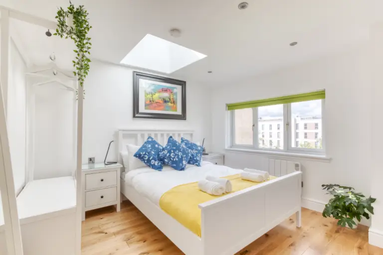 Bright double bedroom with blue cushions and a yellow bed runner