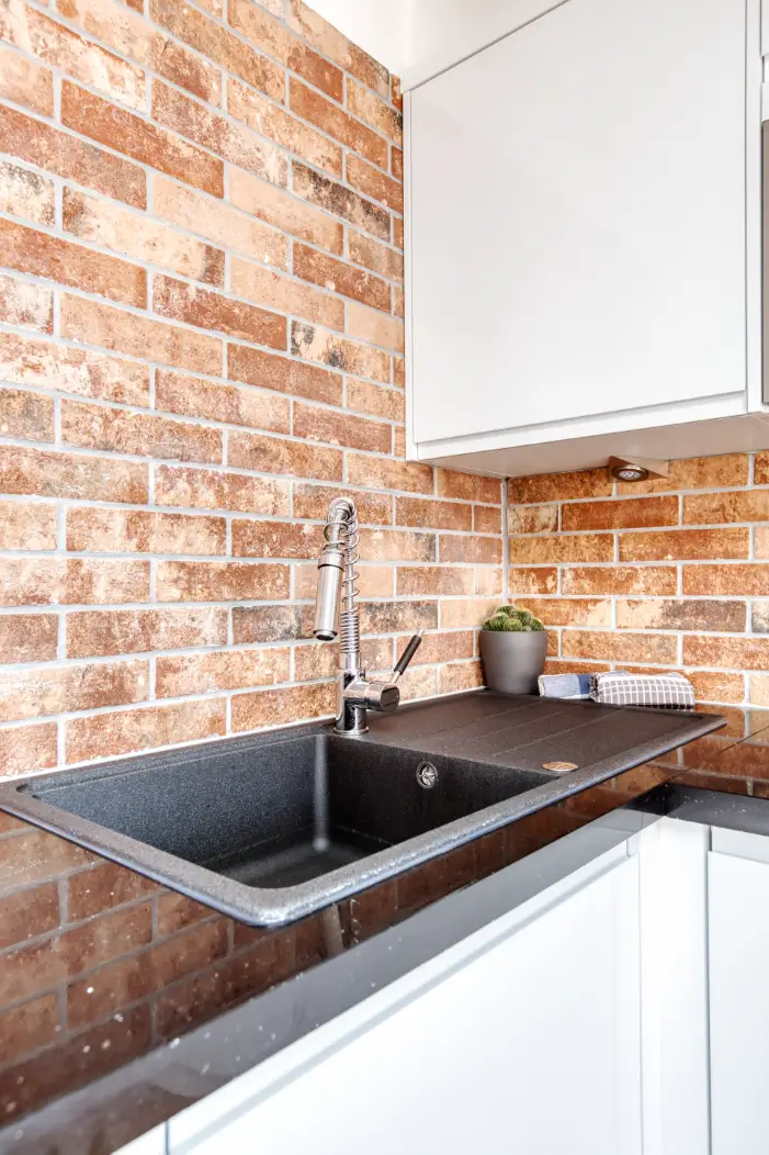 Kitchen sink and white cupboards beside an exposed brick wall
