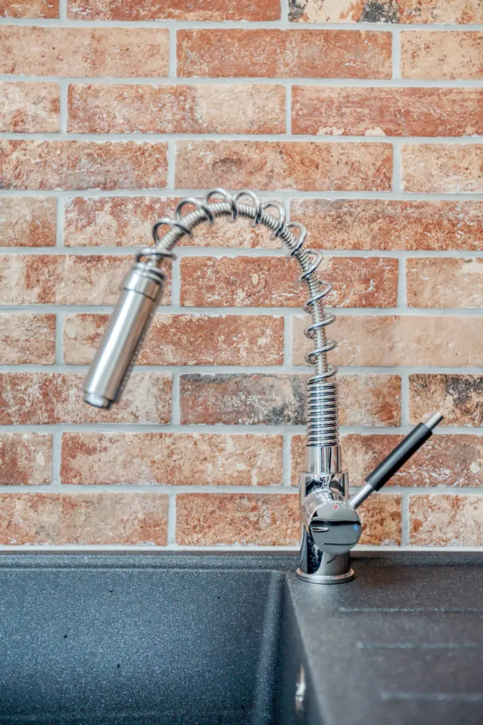 Kitchen tap and dark sink against an exposed brick splashback